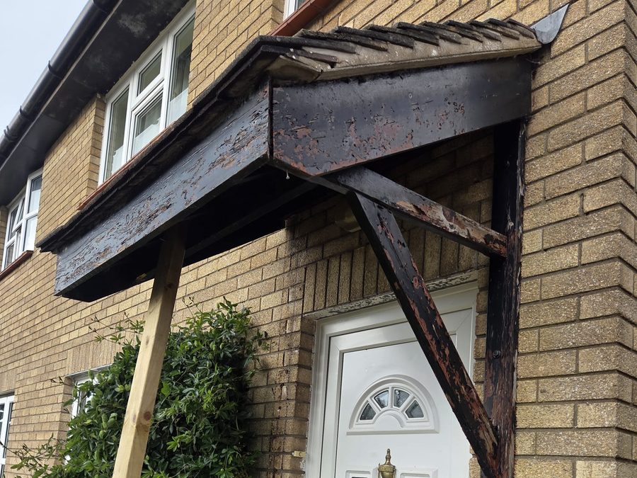 Door canopy with missing and weathered timbers and flaking black paint