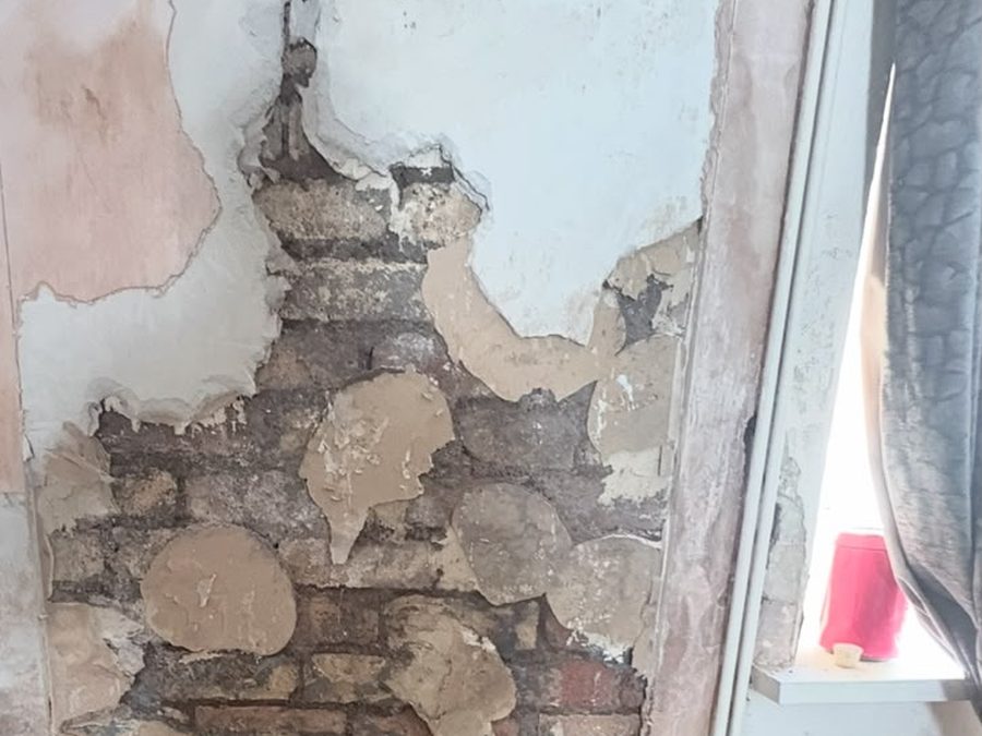 Wall with blown plaster stripped back to brickwork